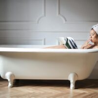 photo of a woman in white bathtub reading magazine