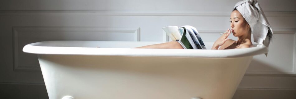 photo of a woman in white bathtub reading magazine