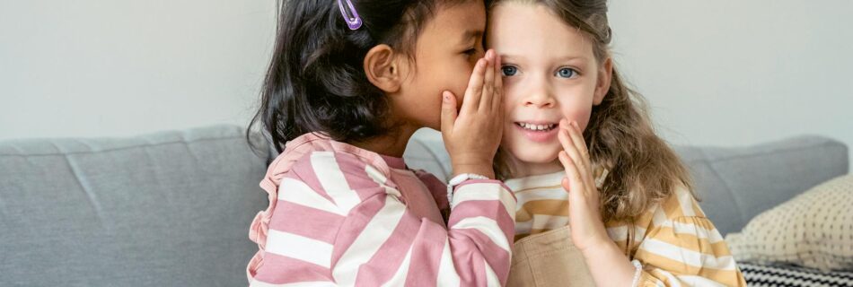 hispanic girl whispering secret on ear of friend